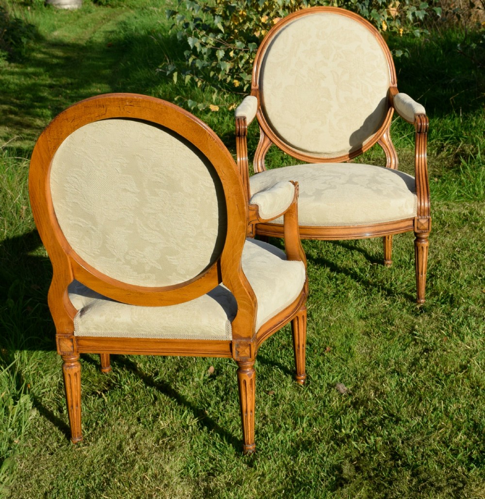 A pair of French Louis XVI style open armchairs featuring carved wooden frames, oval medallion backs, fluted legs, and cream damask upholstery. View IX
