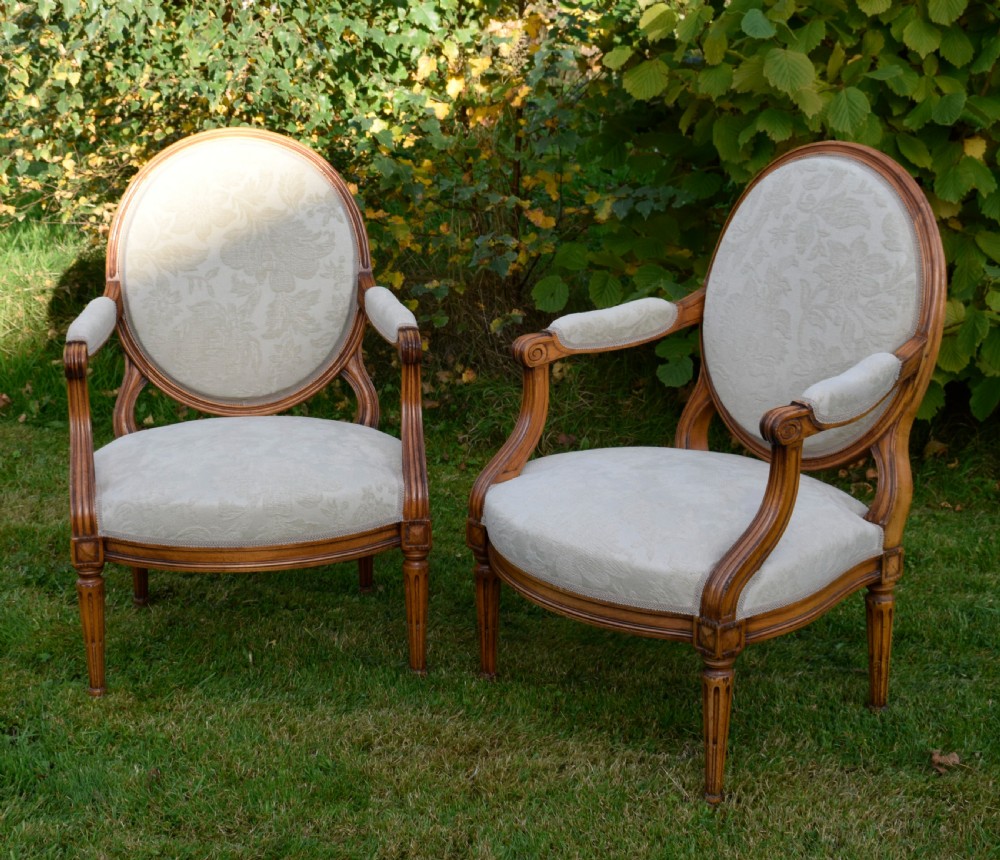 A pair of French Louis XVI style open armchairs featuring carved wooden frames, oval medallion backs, fluted legs, and cream damask upholstery. View XI