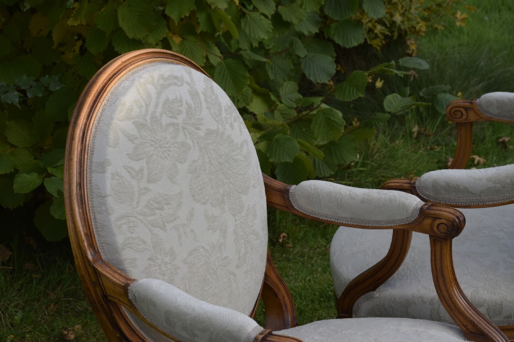 A pair of French Louis XVI style open armchairs featuring carved wooden frames, oval medallion backs, fluted legs, and cream damask upholstery. View XIV