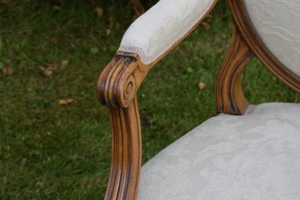 A pair of French Louis XVI style open armchairs featuring carved wooden frames, oval medallion backs, fluted legs, and cream damask upholstery. View XIX