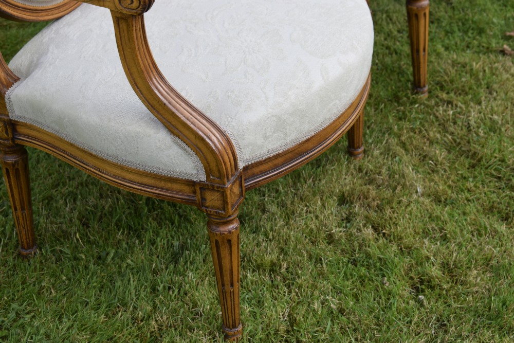 A pair of French Louis XVI style open armchairs featuring carved wooden frames, oval medallion backs, fluted legs, and cream damask upholstery. View XXIV