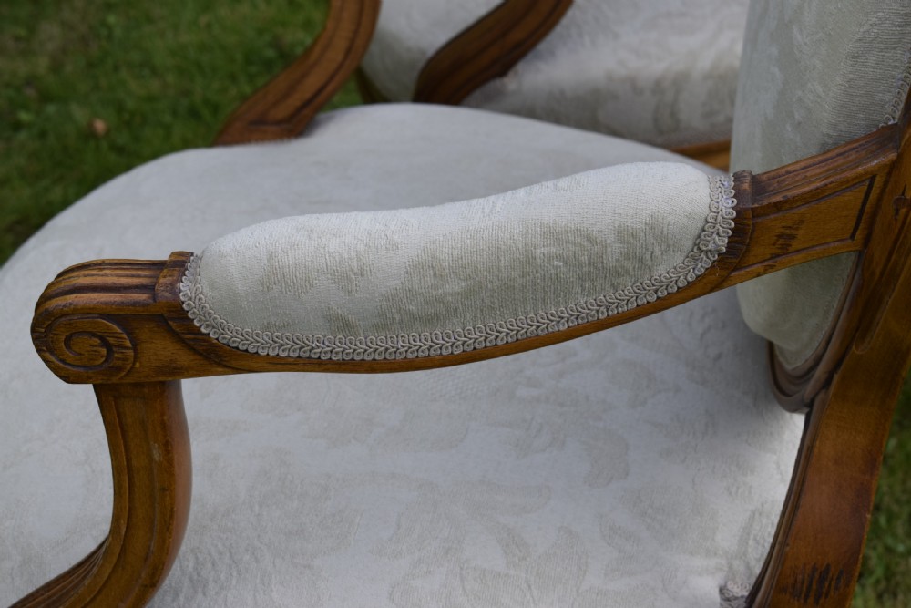 A pair of French Louis XVI style open armchairs featuring carved wooden frames, oval medallion backs, fluted legs, and cream damask upholstery. View XXVII