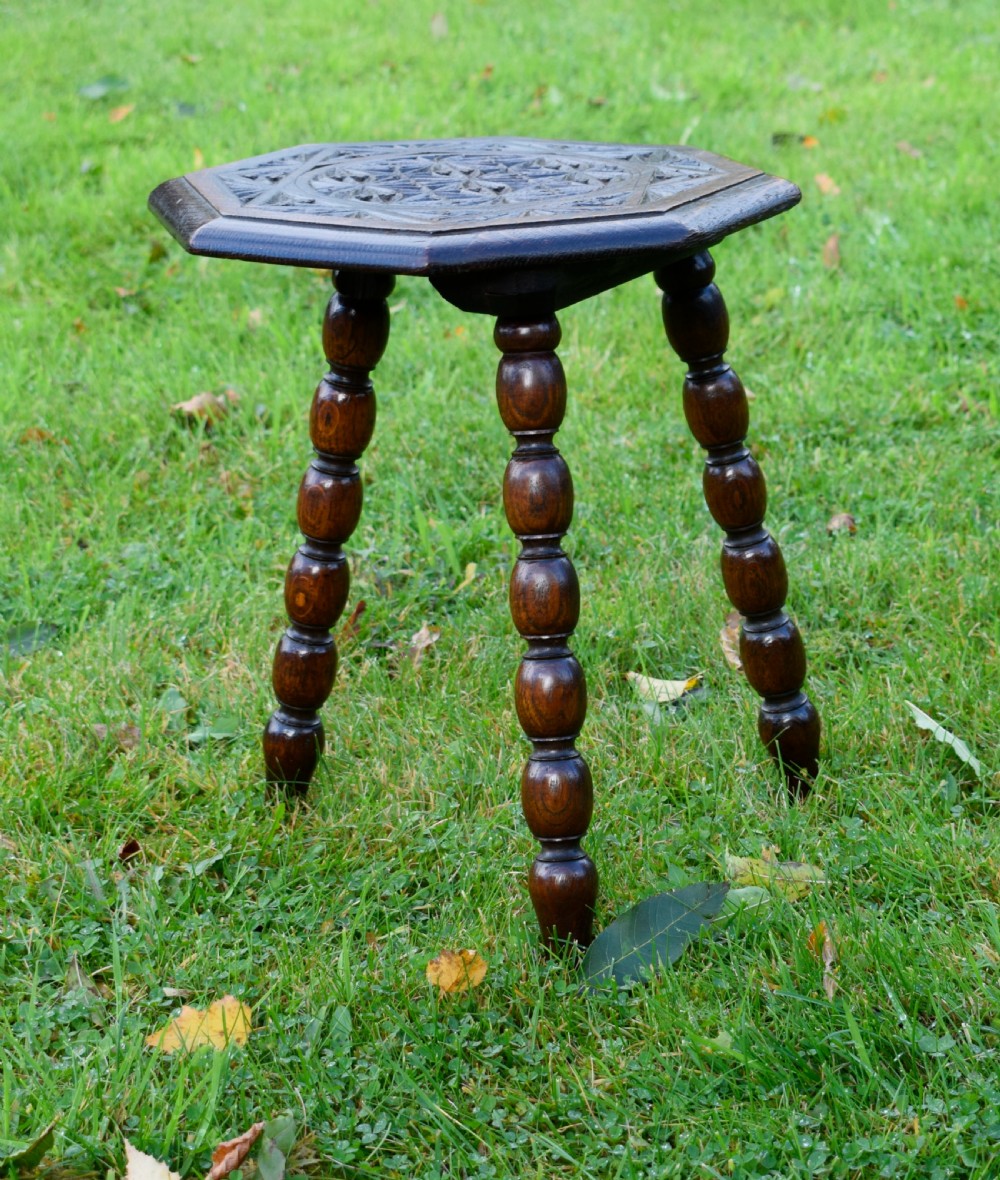 A dark stained wooden side table featuring an octagonal carved geometric top supported by three bobbin-turned legs. View X