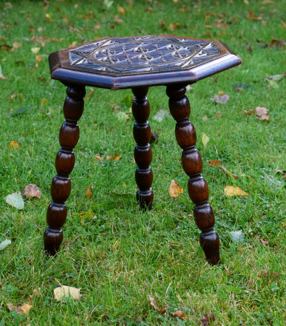 A dark stained wooden side table featuring an octagonal carved geometric top supported by three bobbin-turned legs. View XII