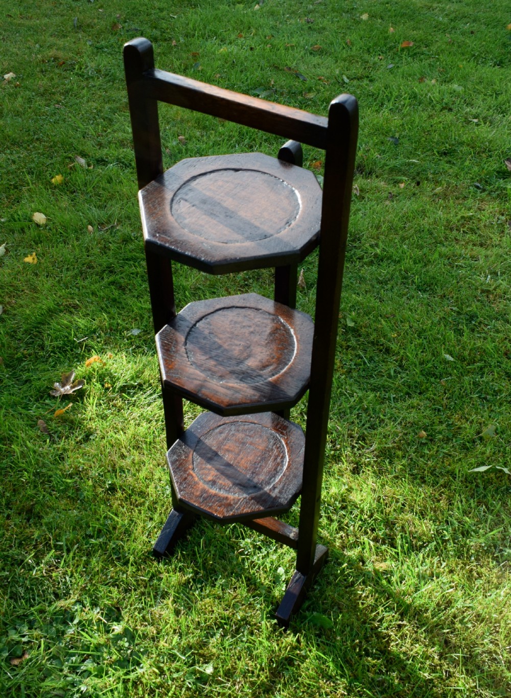 An early 20th-century dark oak three-tier folding cake stand featuring octagonal wooden platforms supported by a slender timber frame. View VII