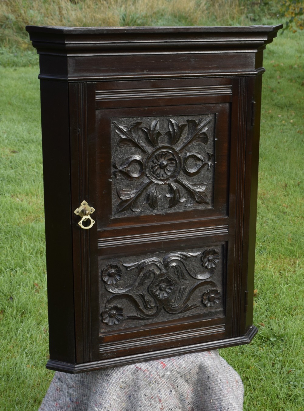 A dark-stained Victorian pine corner cupboard featuring hand-carved foliate panels, a moulded cornice, and a brass latch. View III