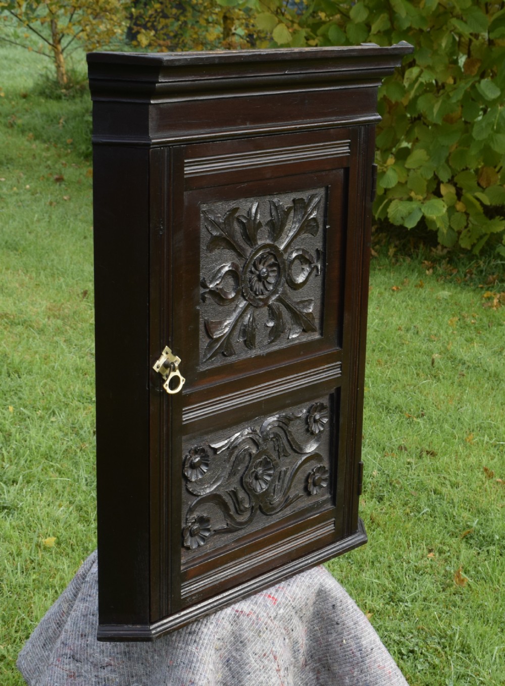 A dark-stained Victorian pine corner cupboard featuring hand-carved foliate panels, a moulded cornice, and a brass latch. View V