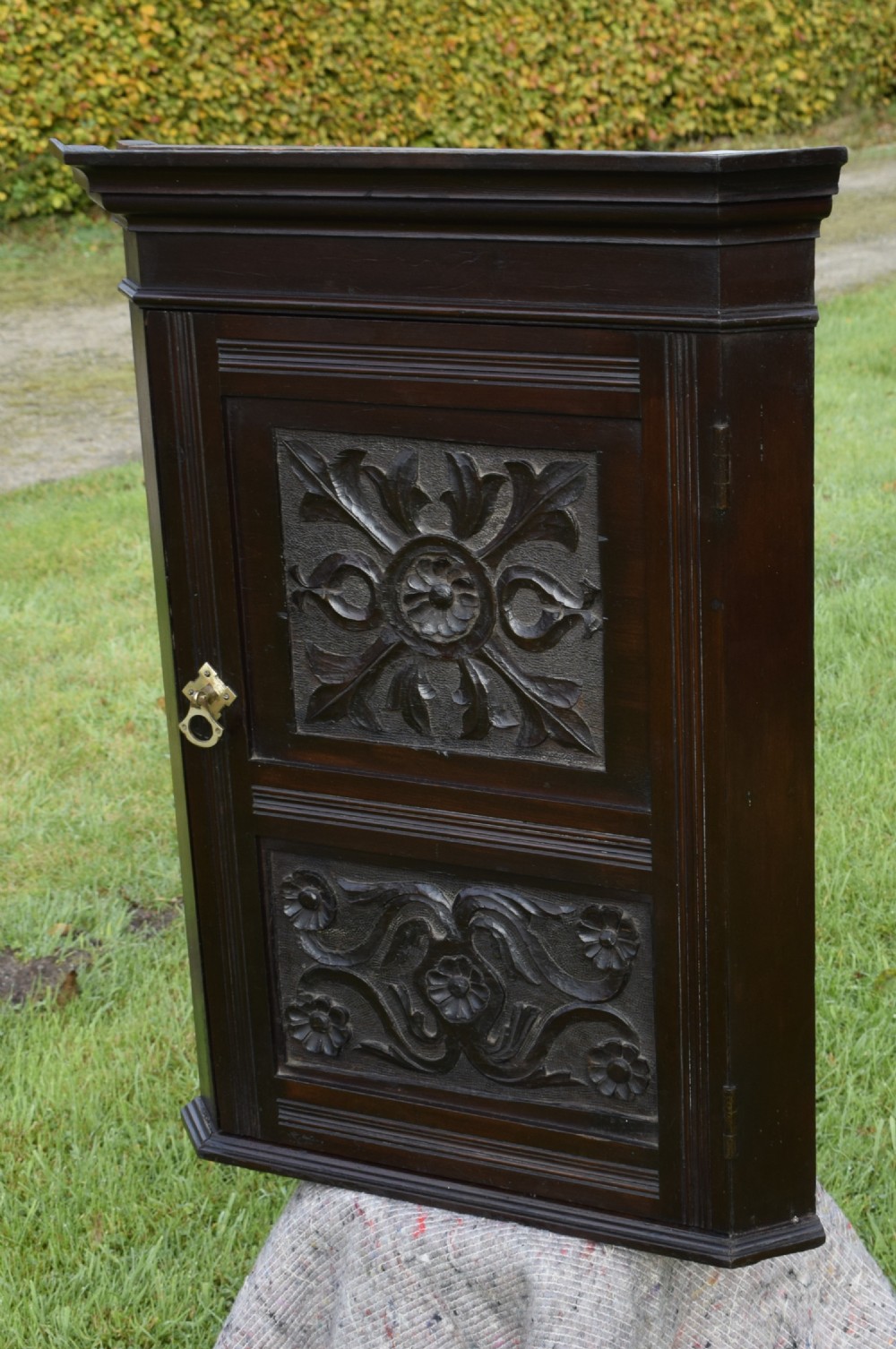 A dark-stained Victorian pine corner cupboard featuring hand-carved foliate panels, a moulded cornice, and a brass latch. View VI