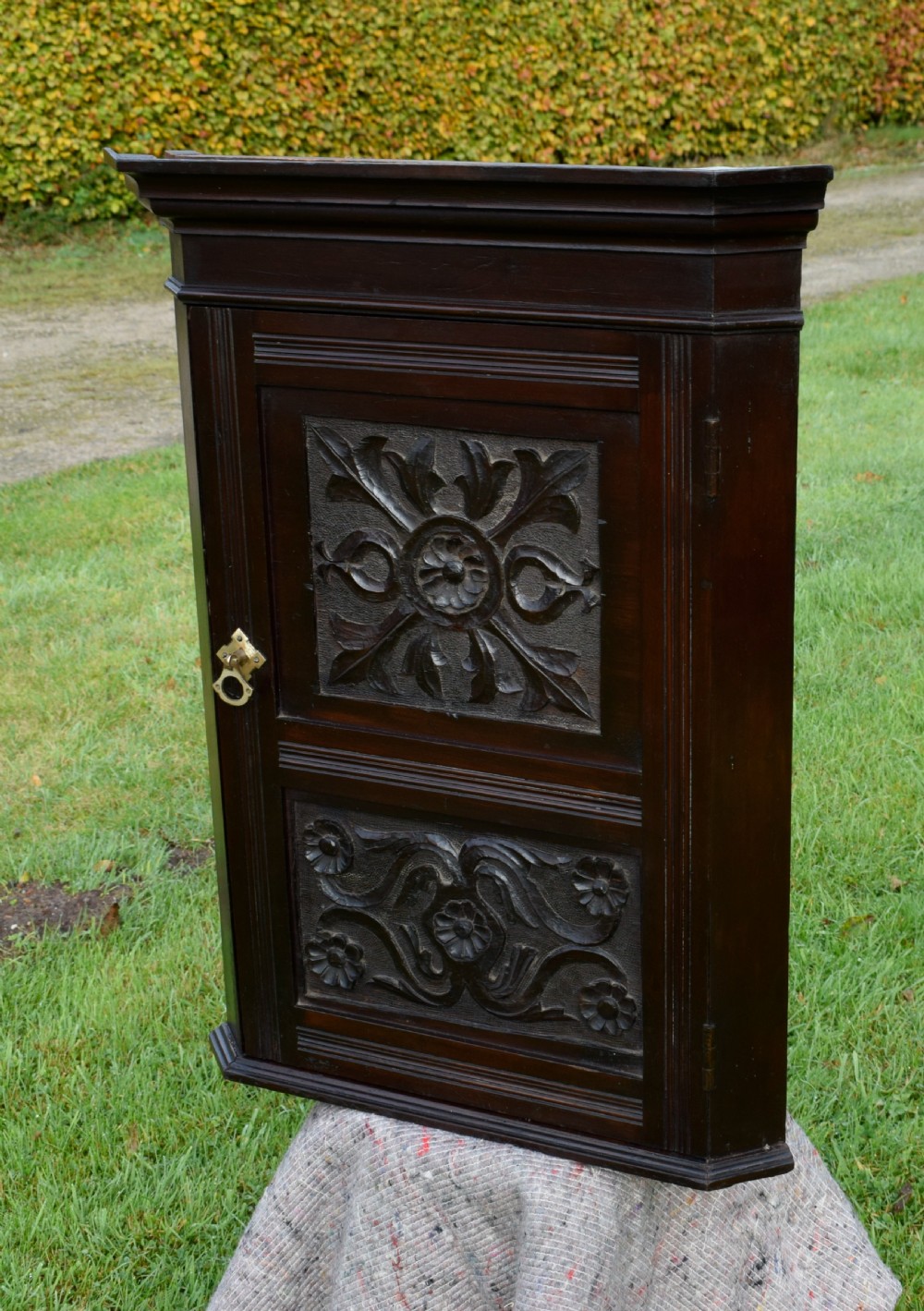 A dark-stained Victorian pine corner cupboard featuring hand-carved foliate panels, a moulded cornice, and a brass latch. View VII