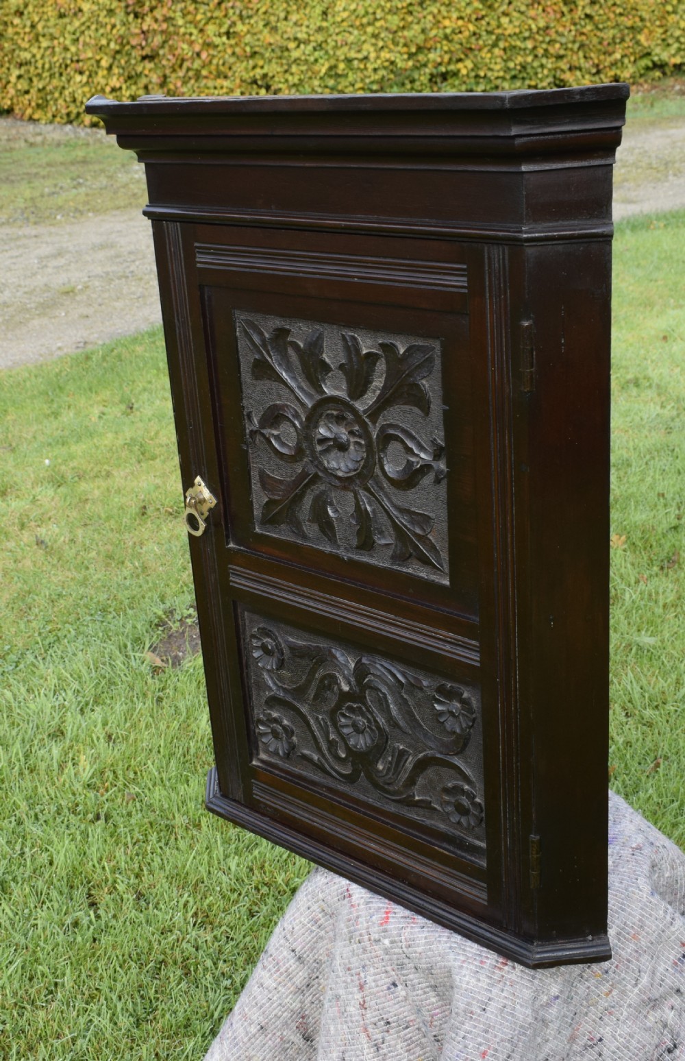 A dark-stained Victorian pine corner cupboard featuring hand-carved foliate panels, a moulded cornice, and a brass latch. View X