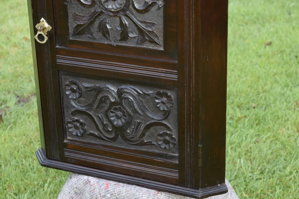 A dark-stained Victorian pine corner cupboard featuring hand-carved foliate panels, a moulded cornice, and a brass latch. View XI