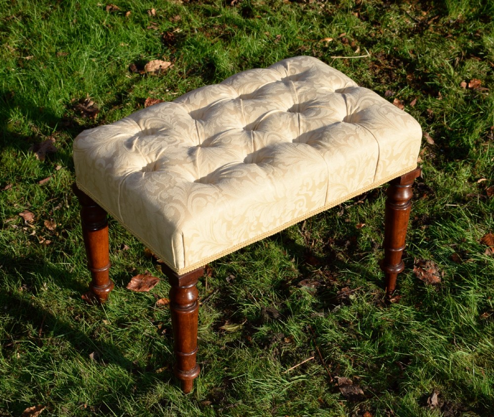 A Victorian upholstered rectangular footstool featuring cream damask fabric with deep buttoning, braid trim, and four dark turned wooden legs. View II