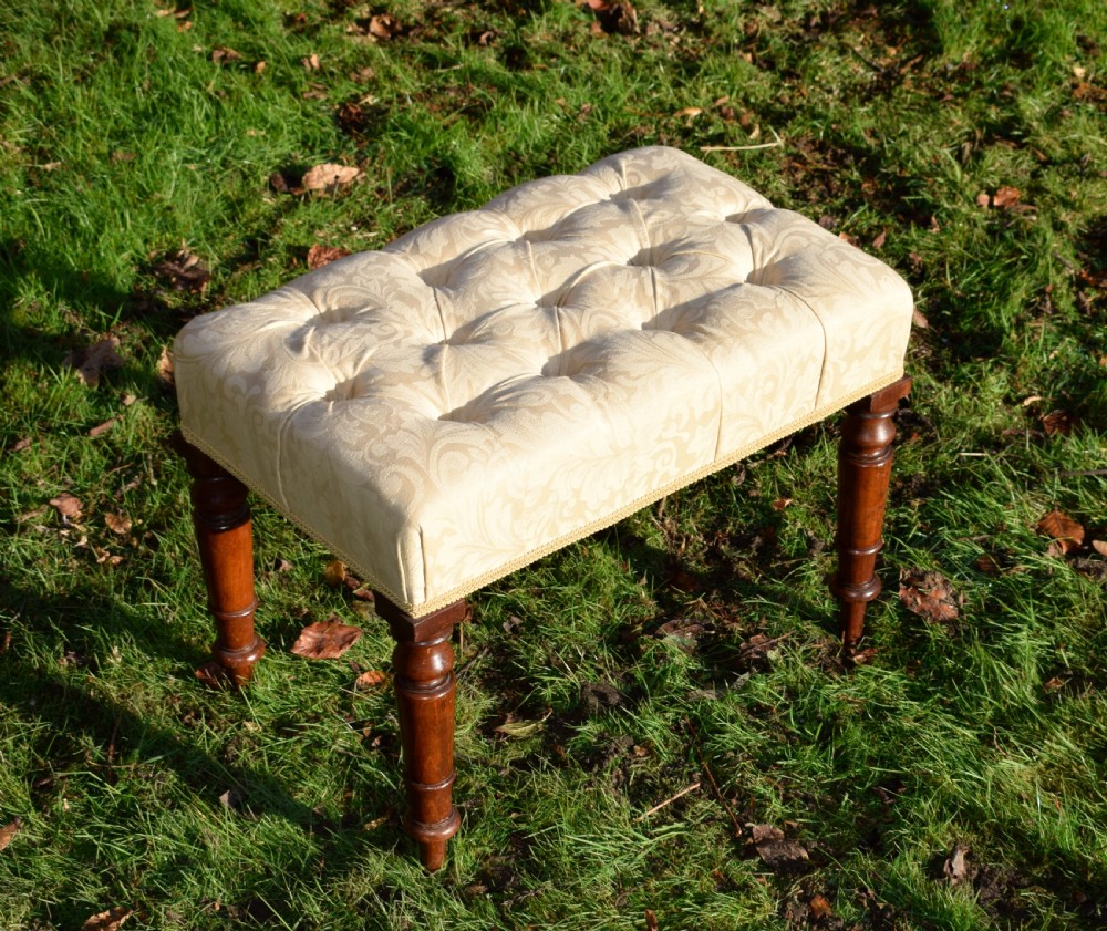 A Victorian upholstered rectangular footstool featuring cream damask fabric with deep buttoning, braid trim, and four dark turned wooden legs. View III