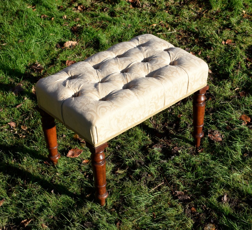 A Victorian upholstered rectangular footstool featuring cream damask fabric with deep buttoning, braid trim, and four dark turned wooden legs. View IV