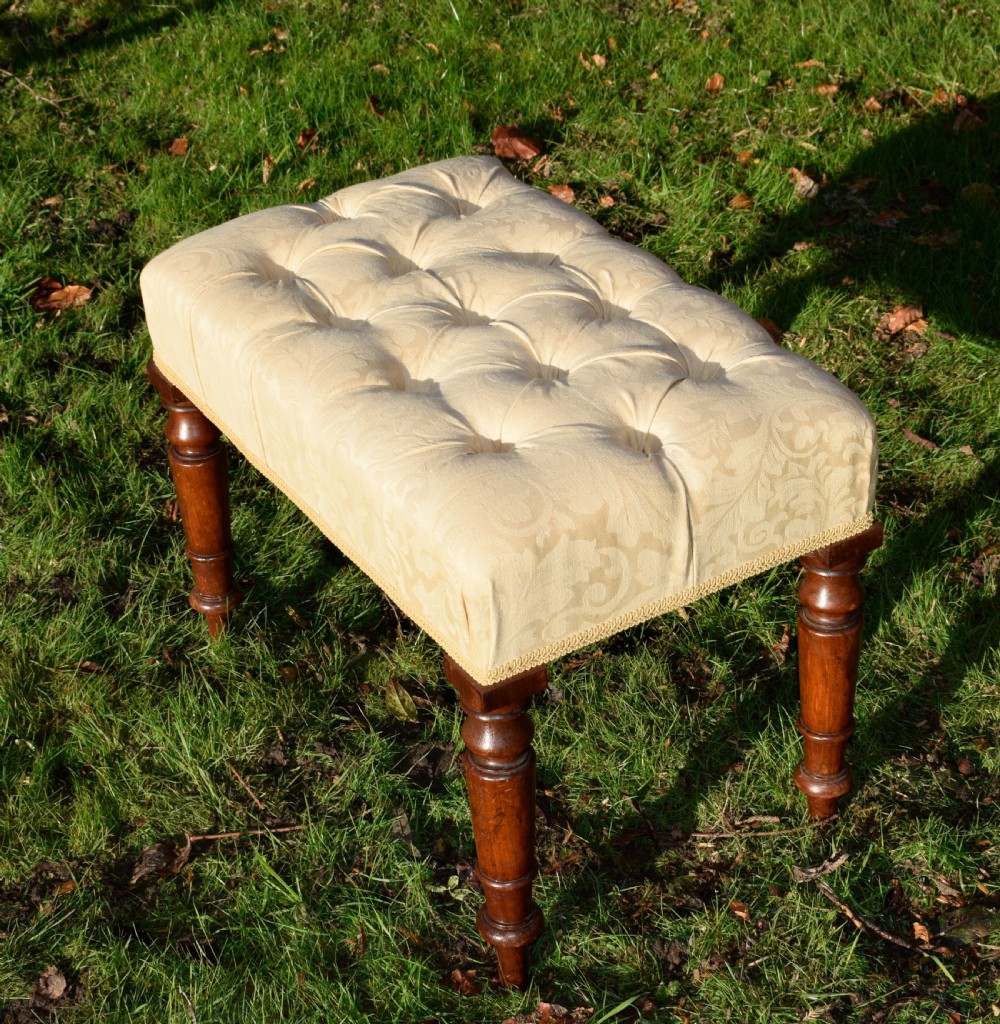 A Victorian upholstered rectangular footstool featuring cream damask fabric with deep buttoning, braid trim, and four dark turned wooden legs. View V