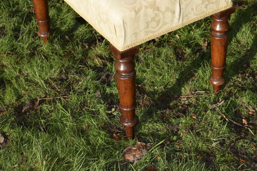 A Victorian upholstered rectangular footstool featuring cream damask fabric with deep buttoning, braid trim, and four dark turned wooden legs. View VII