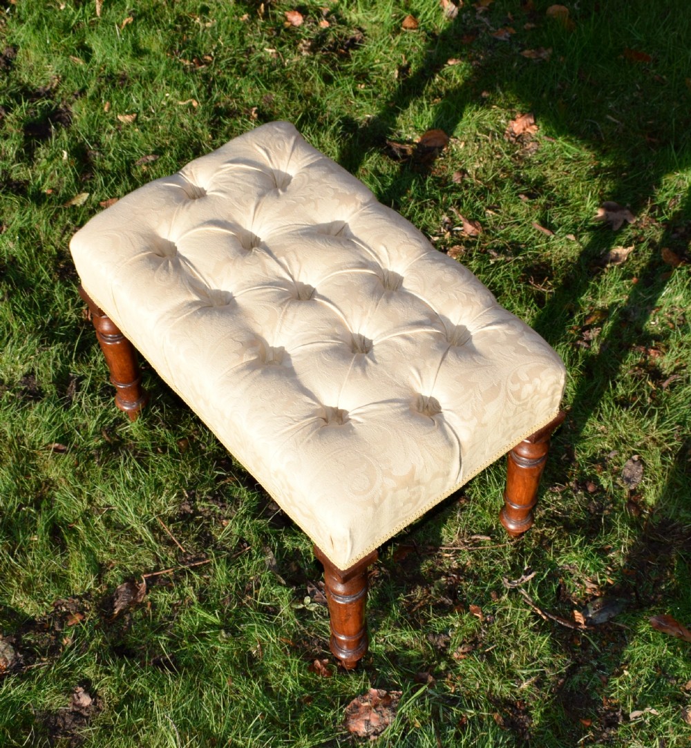 A Victorian upholstered rectangular footstool featuring cream damask fabric with deep buttoning, braid trim, and four dark turned wooden legs. View VIII