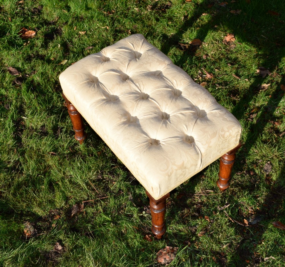 A Victorian upholstered rectangular footstool featuring cream damask fabric with deep buttoning, braid trim, and four dark turned wooden legs. View IX