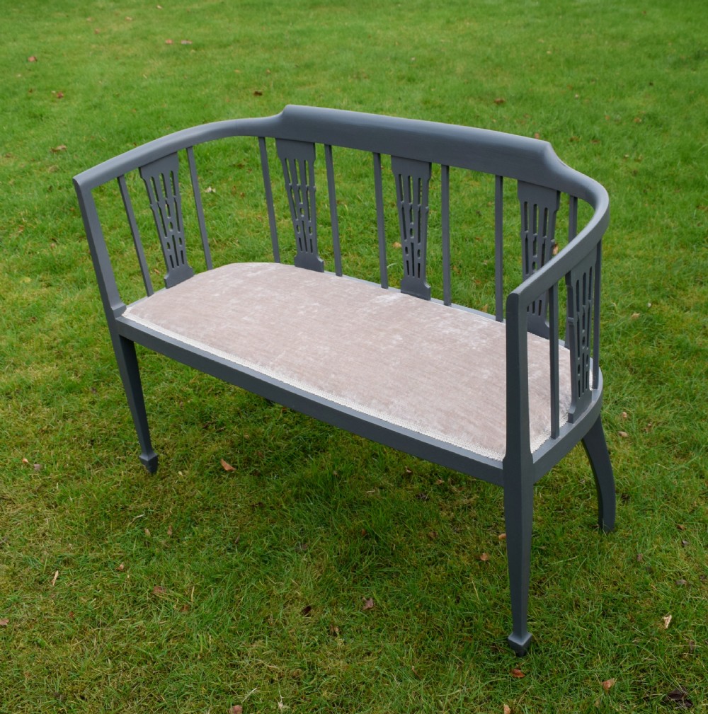 An Edwardian painted grey wooden settee featuring vertical spindles, pierced back splats, and a neutral beige velvet upholstered seat. View III