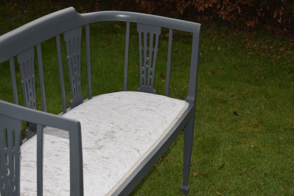 An Edwardian painted grey wooden settee featuring vertical spindles, pierced back splats, and a neutral beige velvet upholstered seat. View IV