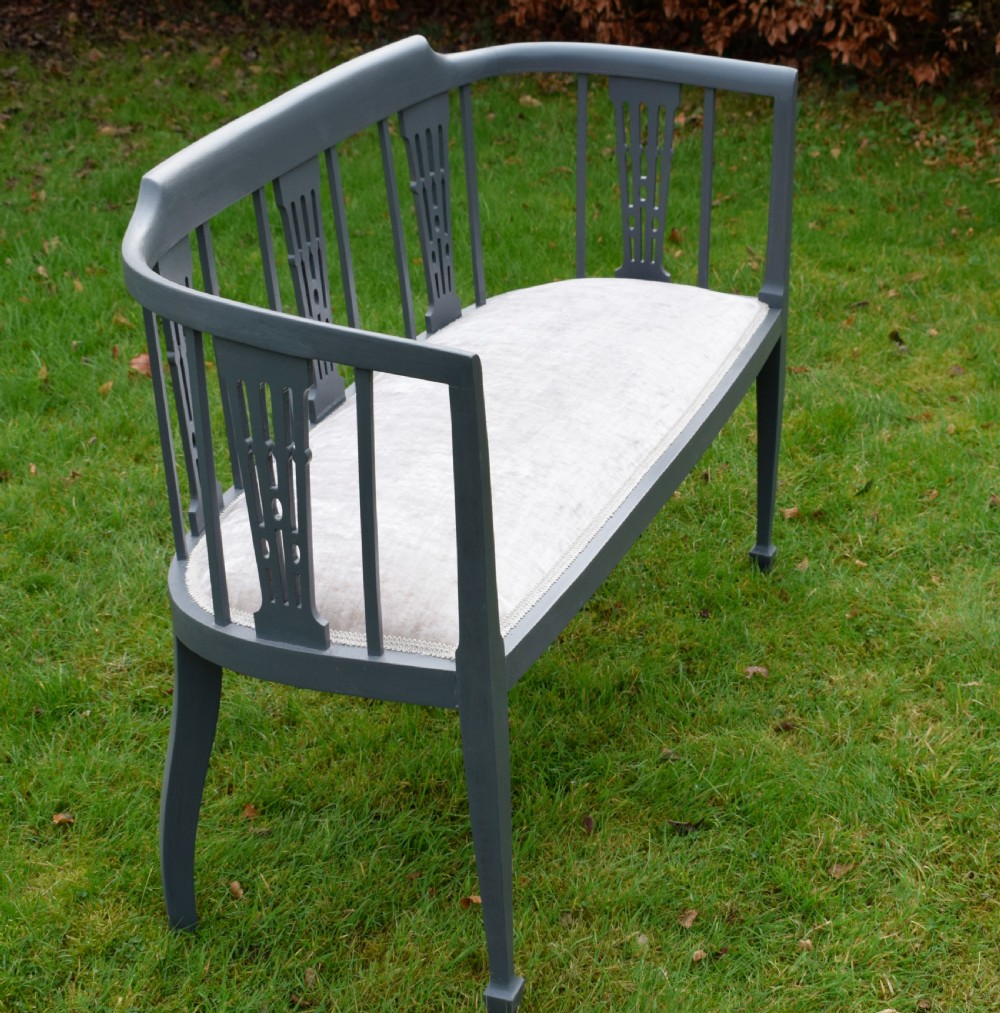 An Edwardian painted grey wooden settee featuring vertical spindles, pierced back splats, and a neutral beige velvet upholstered seat. View V