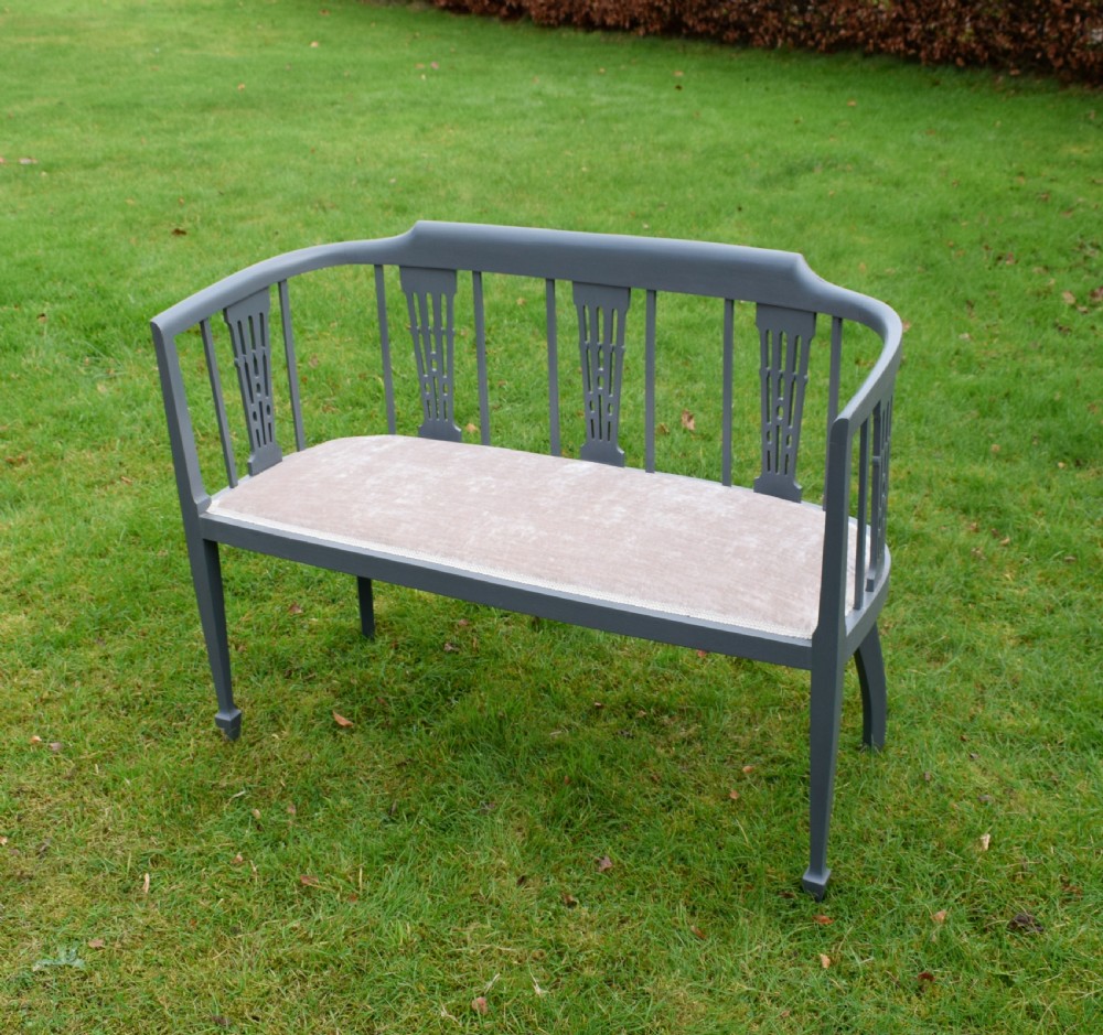 An Edwardian painted grey wooden settee featuring vertical spindles, pierced back splats, and a neutral beige velvet upholstered seat. View VI