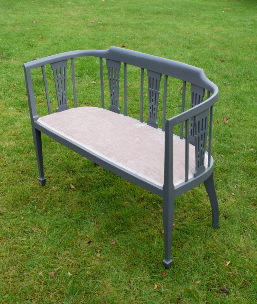 An Edwardian painted grey wooden settee featuring vertical spindles, pierced back splats, and a neutral beige velvet upholstered seat. View VII