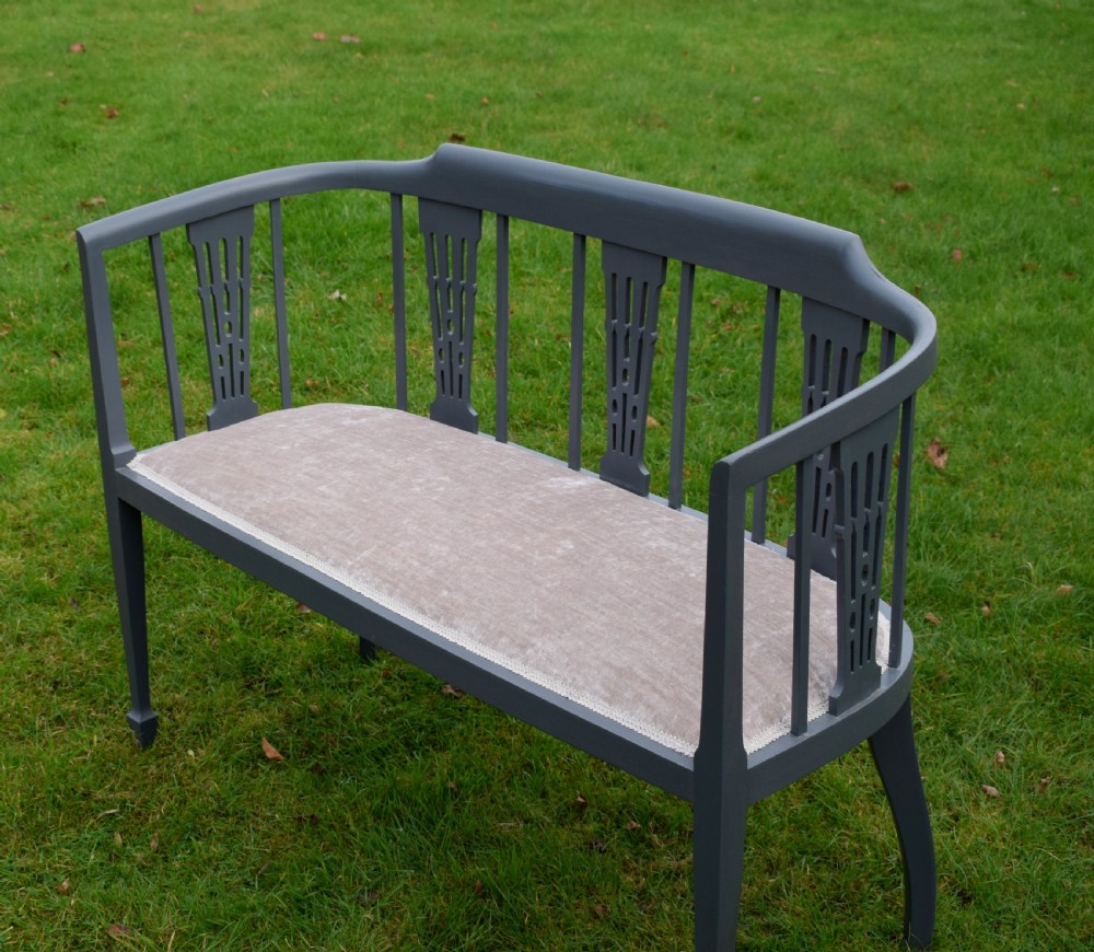 An Edwardian painted grey wooden settee featuring vertical spindles, pierced back splats, and a neutral beige velvet upholstered seat. View VIII