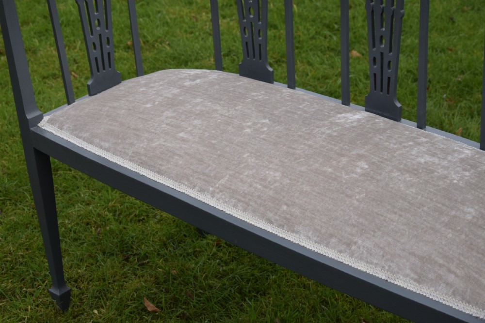An Edwardian painted grey wooden settee featuring vertical spindles, pierced back splats, and a neutral beige velvet upholstered seat. View IX