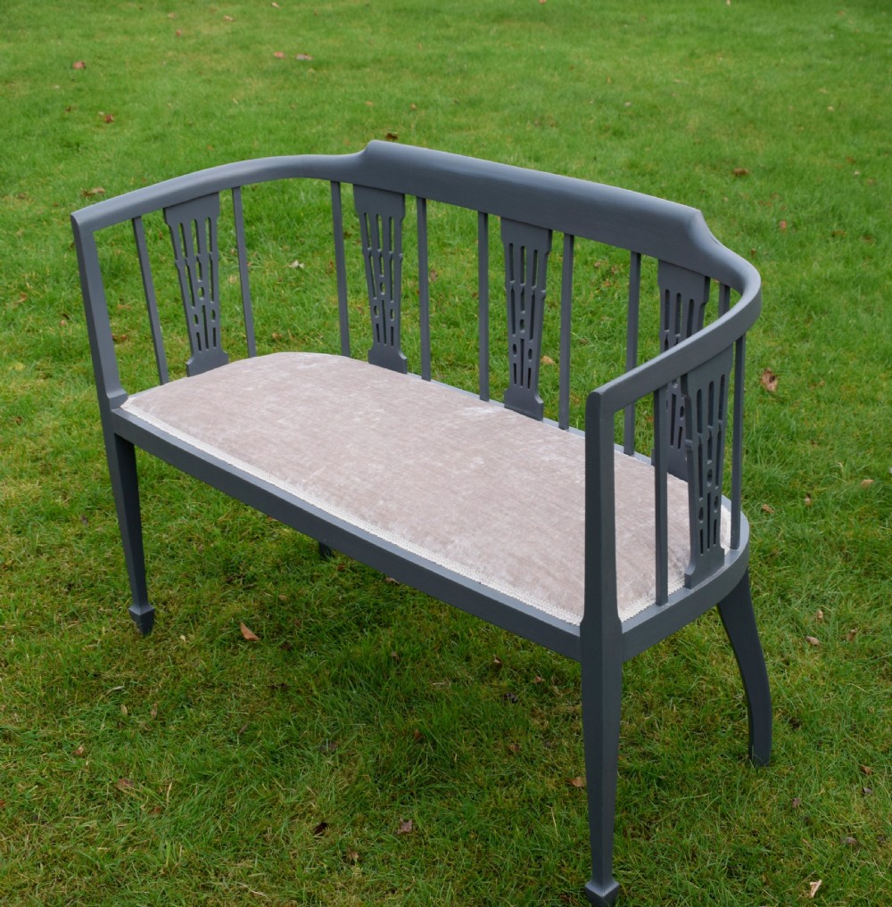 An Edwardian painted grey wooden settee featuring vertical spindles, pierced back splats, and a neutral beige velvet upholstered seat. View XI