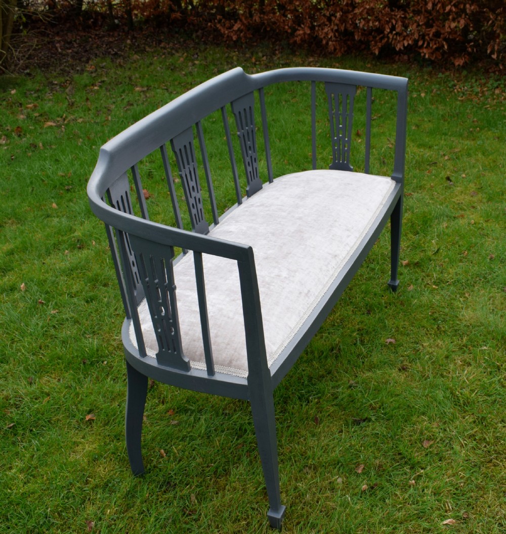 An Edwardian painted grey wooden settee featuring vertical spindles, pierced back splats, and a neutral beige velvet upholstered seat. View XII