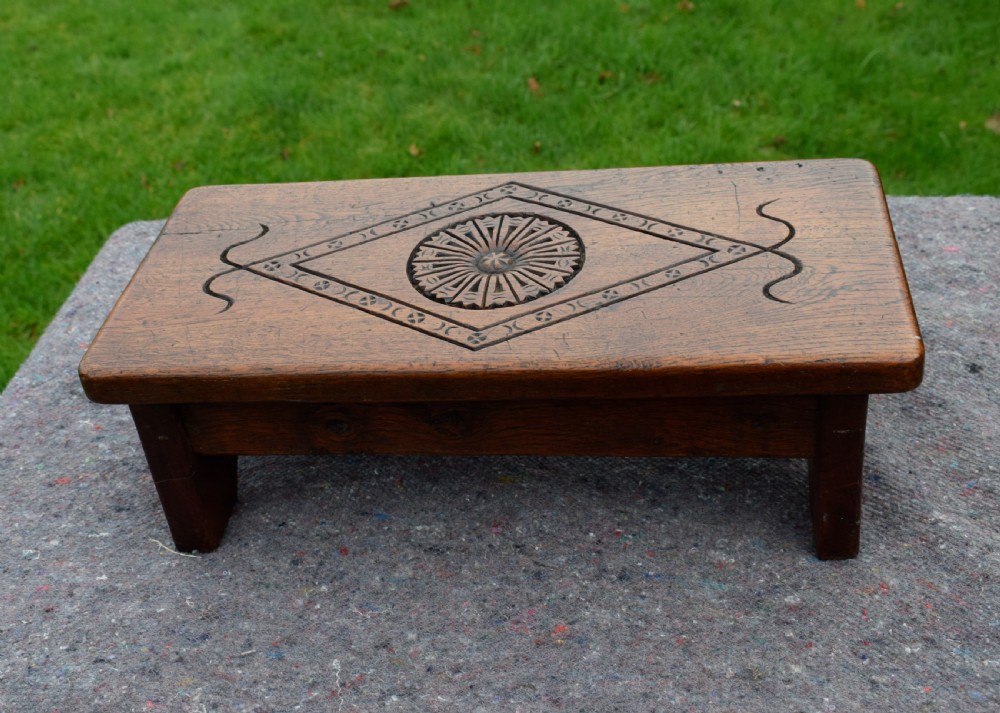 A rectangular warm brown carved oak footstool featuring a central rosette enclosed in a lozenge motif set upon slab legs. View III