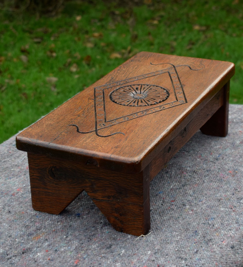 A rectangular warm brown carved oak footstool featuring a central rosette enclosed in a lozenge motif set upon slab legs. View V