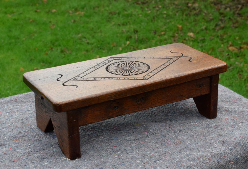 A rectangular warm brown carved oak footstool featuring a central rosette enclosed in a lozenge motif set upon slab legs. View VI