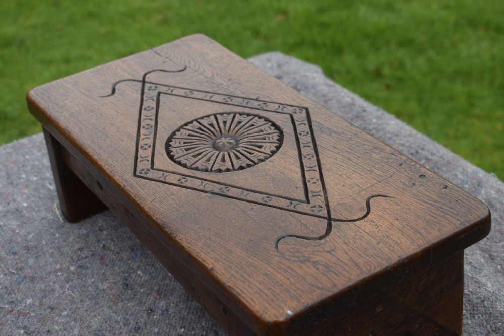A rectangular warm brown carved oak footstool featuring a central rosette enclosed in a lozenge motif set upon slab legs. View VIII