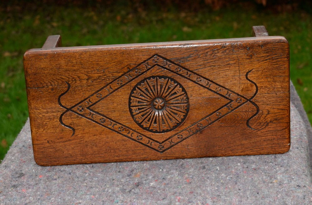 A rectangular warm brown carved oak footstool featuring a central rosette enclosed in a lozenge motif set upon slab legs. View XII
