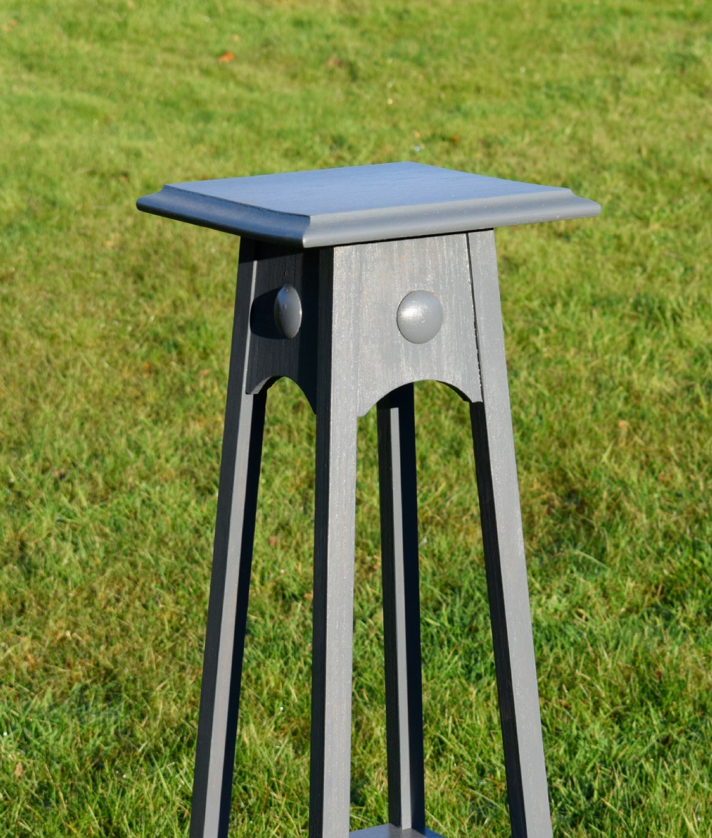 A tall grey painted Arts and Crafts wooden jardiniere stand featuring a square top, arched aprons with circular boss details, tapered legs, and a lower shelf. View VIII