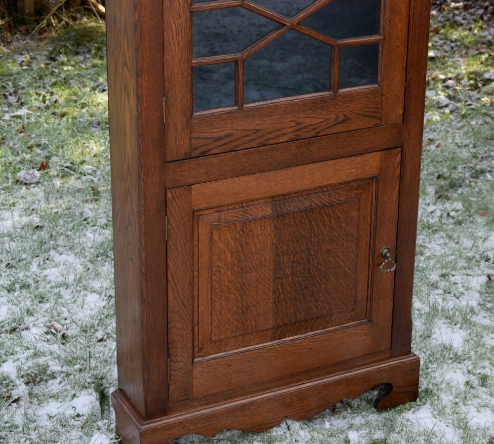 An early twentieth-century freestanding oak corner cabinet featuring an upper astragal glazed door and a lower solid panelled door on bracket feet. View III