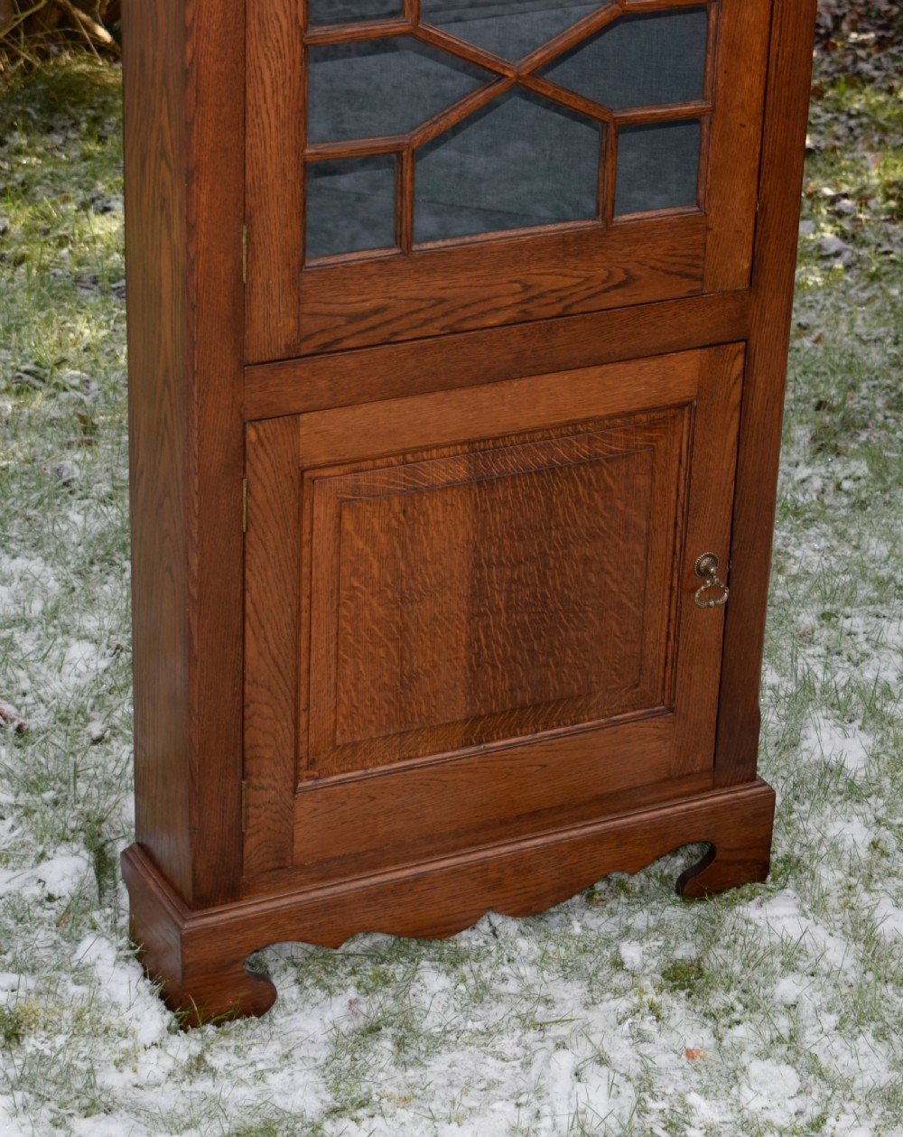 An early twentieth-century freestanding oak corner cabinet featuring an upper astragal glazed door and a lower solid panelled door on bracket feet. View IV