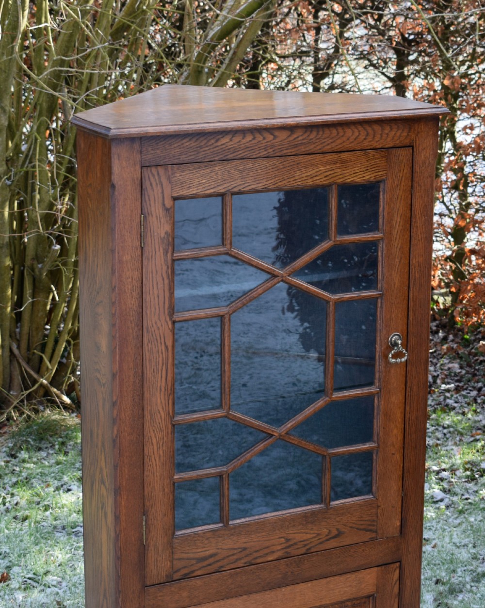 An early twentieth-century freestanding oak corner cabinet featuring an upper astragal glazed door and a lower solid panelled door on bracket feet. View V