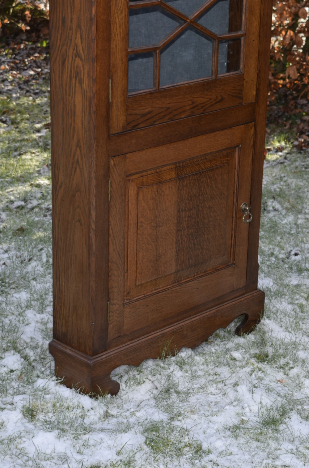 An early twentieth-century freestanding oak corner cabinet featuring an upper astragal glazed door and a lower solid panelled door on bracket feet. View X