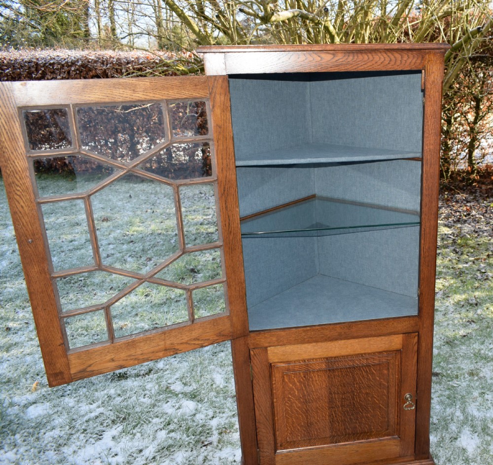 An early twentieth-century freestanding oak corner cabinet featuring an upper astragal glazed door and a lower solid panelled door on bracket feet. View XII