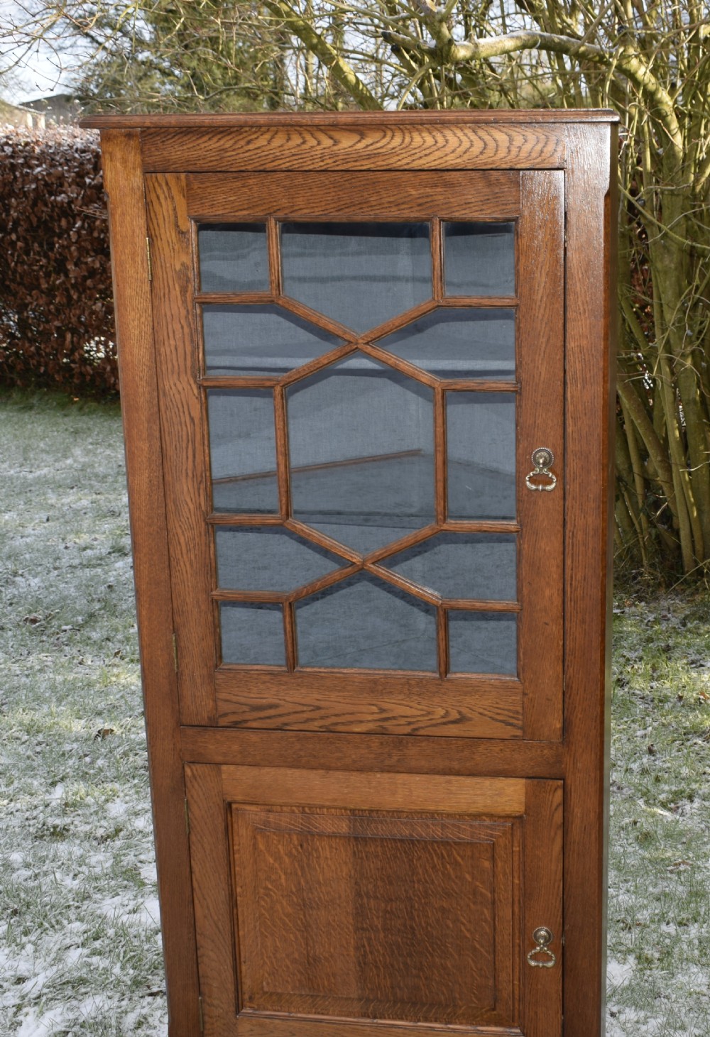 An early twentieth-century freestanding oak corner cabinet featuring an upper astragal glazed door and a lower solid panelled door on bracket feet. View XX
