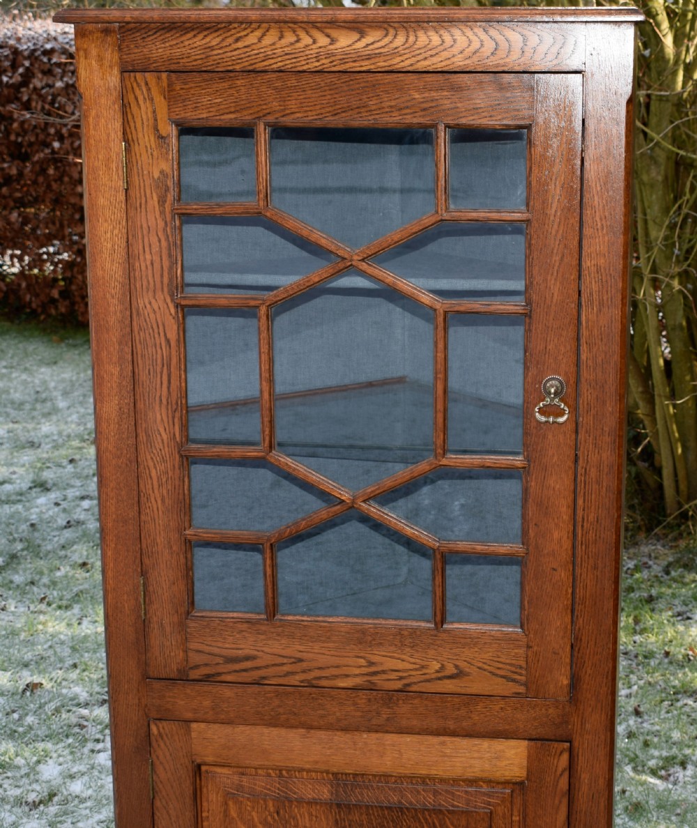 An early twentieth-century freestanding oak corner cabinet featuring an upper astragal glazed door and a lower solid panelled door on bracket feet. View XXI
