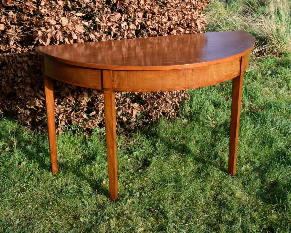 A Georgian mahogany demi-lune console table featuring a semi-circular top with string inlay and three tapered legs.