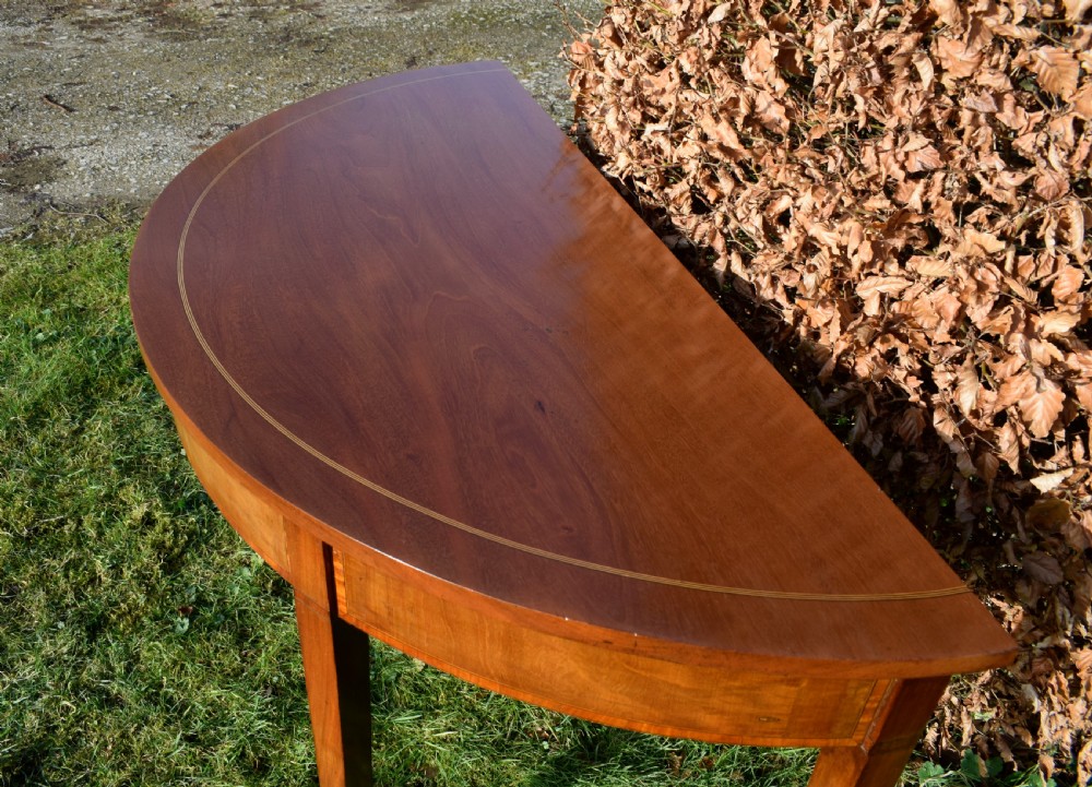 A Georgian mahogany demi-lune console table featuring a semi-circular top with string inlay and three tapered legs. View II