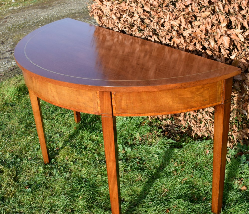 A Georgian mahogany demi-lune console table featuring a semi-circular top with string inlay and three tapered legs. View VI
