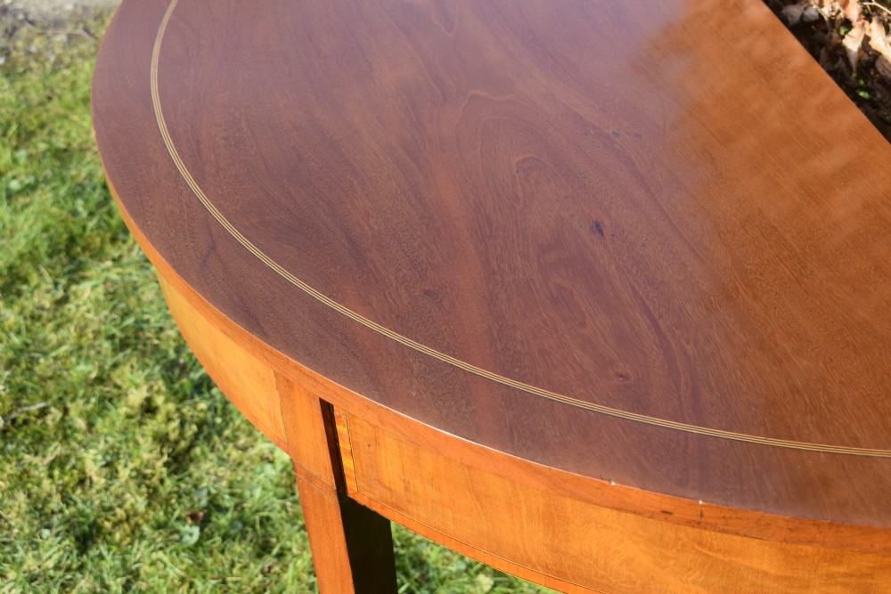 A Georgian mahogany demi-lune console table featuring a semi-circular top with string inlay and three tapered legs. View VII