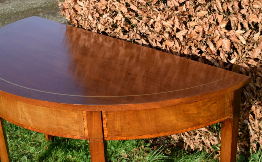 A Georgian mahogany demi-lune console table featuring a semi-circular top with string inlay and three tapered legs. View IX