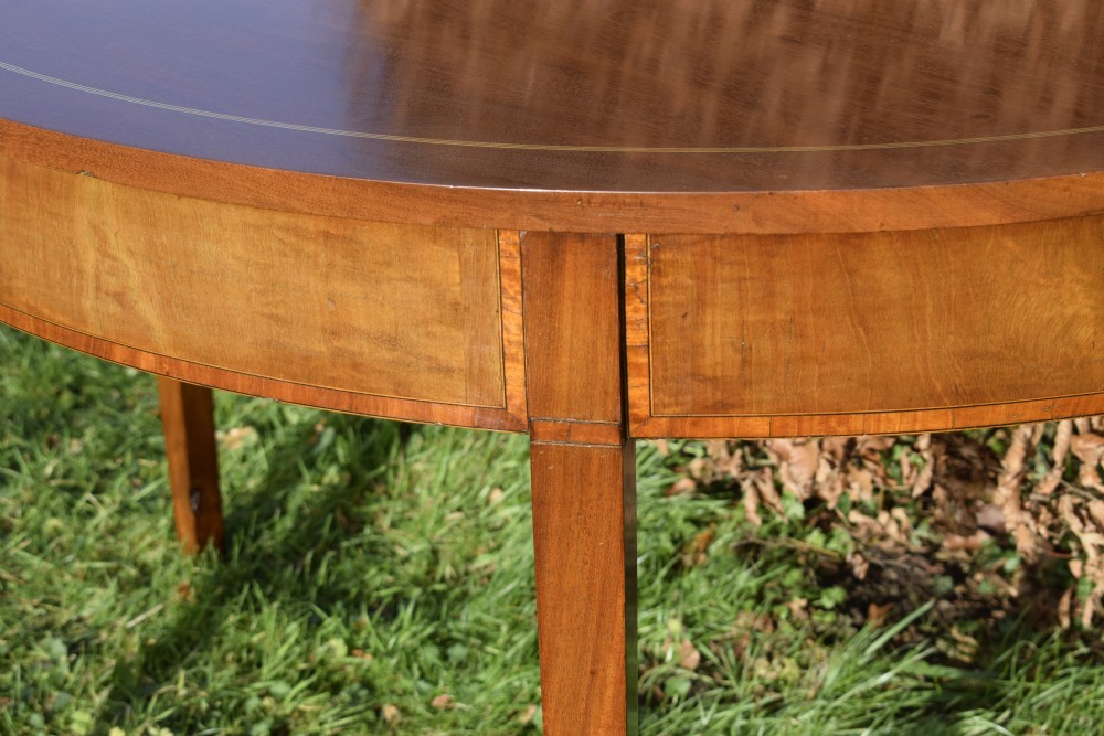 A Georgian mahogany demi-lune console table featuring a semi-circular top with string inlay and three tapered legs. View X